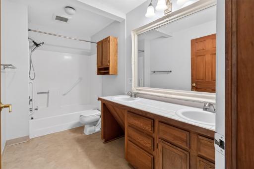 Large bathroom features an expansive double vanity with plenty of storage, an oversized framed mirror, and a clean tub/shower combo with built-in grab bars.