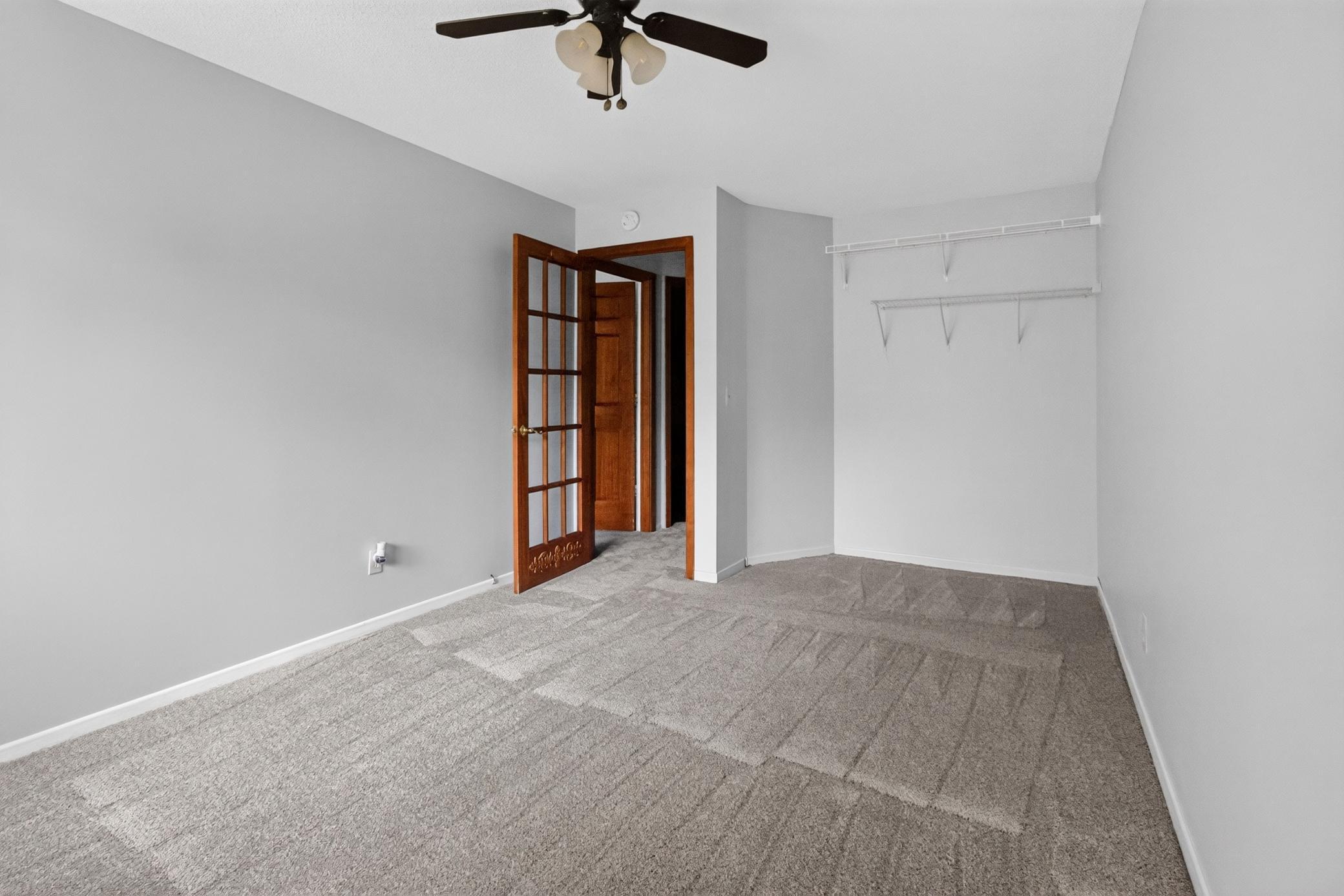 Another spacious bedroom offering a ceiling fan, wire shelving for flexible organization, and an elegant glass-paneled French door.