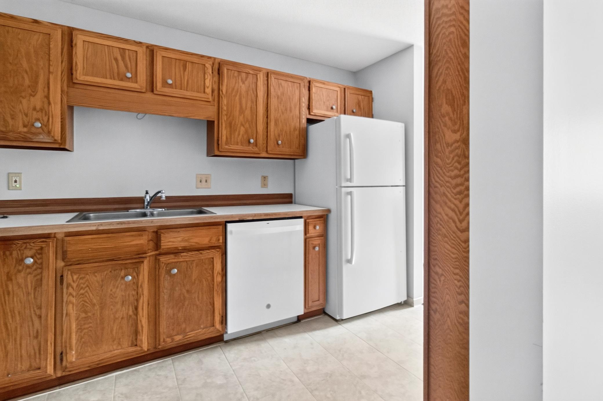 The kitchen features a double-basin stainless steel sink, a built-in white dishwasher, a full-sized refrigerator, and extensive upper and lower cabinet storage.