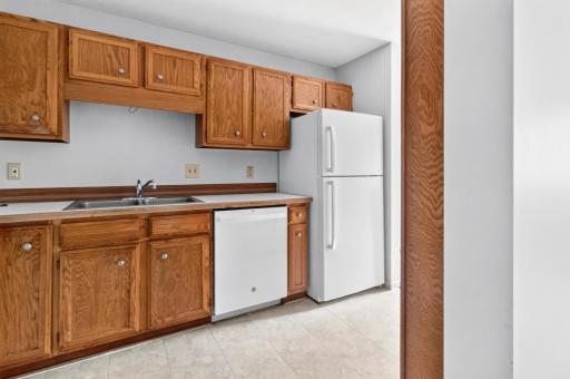 The kitchen features a double-basin stainless steel sink, a built-in white dishwasher, a full-sized refrigerator, and extensive upper and lower cabinet storage.