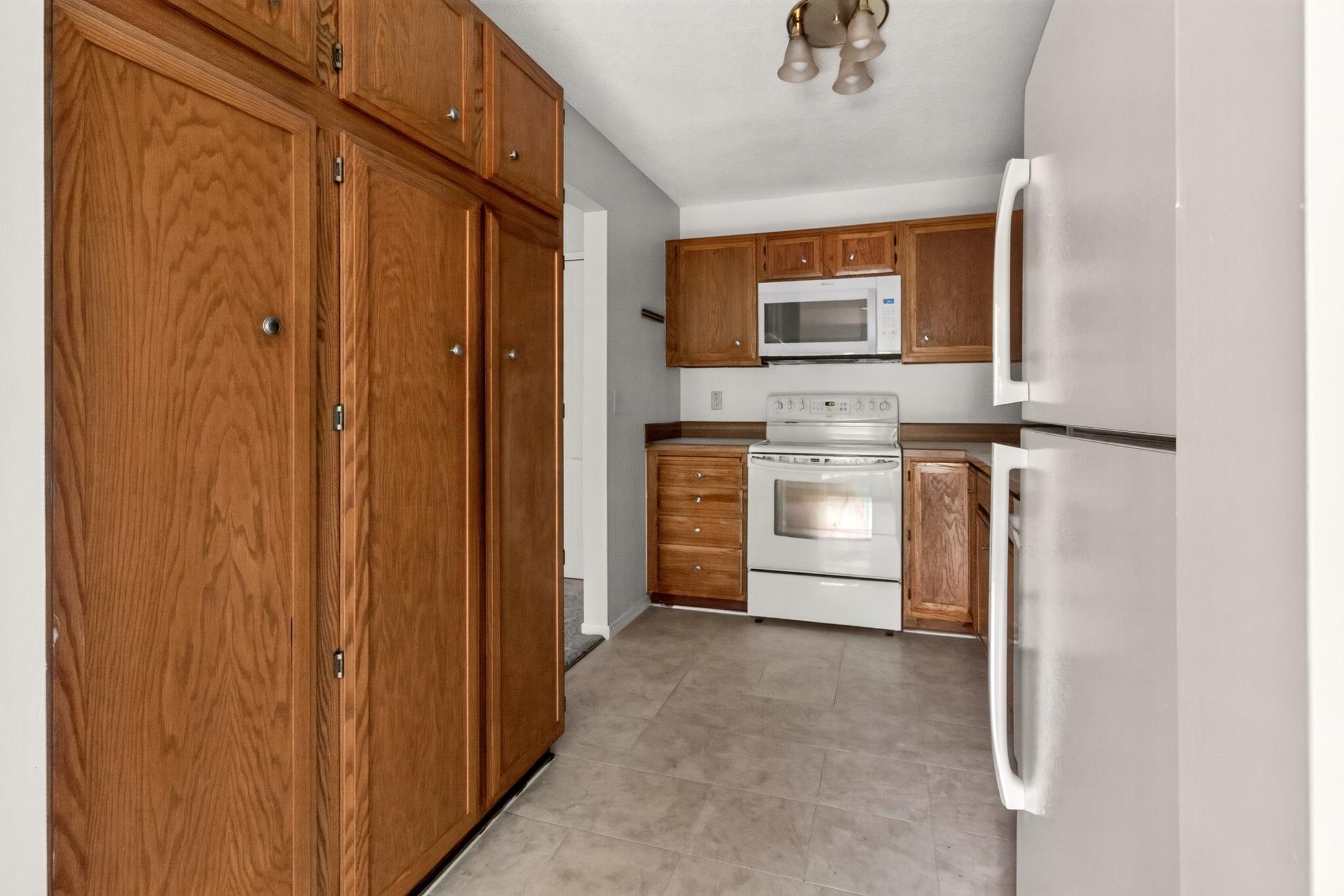 Efficient galley kitchen boasts ample warm oak cabinetry, abundant pantry storage space, a white stove, and an overhead built-in microwave.