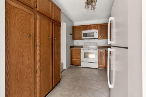 Efficient galley kitchen boasts ample warm oak cabinetry, abundant pantry storage space, a white stove, and an overhead built-in microwave.
