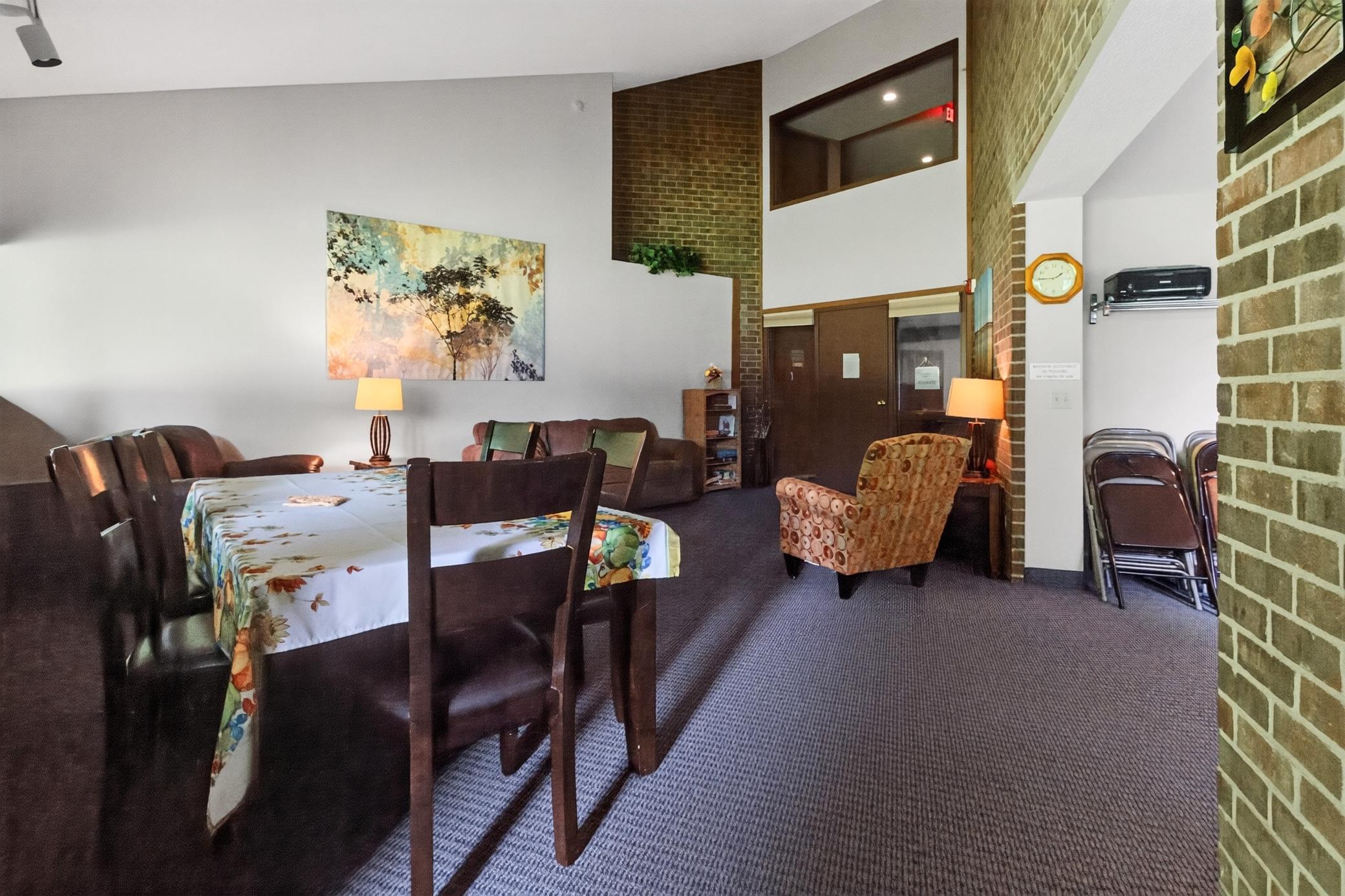 Spacious community room offers a wonderful extended living space for residents, featuring high ceilings, comfortable seating, and a large table for gatherings.