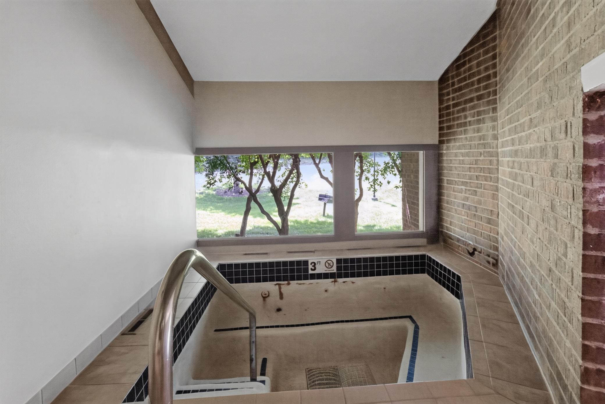 Unwind year-round in the building's indoor hot tub room, featuring an integrated brick accent wall and large viewing windows overlooking the outdoor grounds.