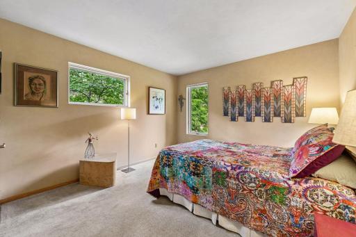 A bright main-level bedroom features soft carpeting and peaceful views of greenery.