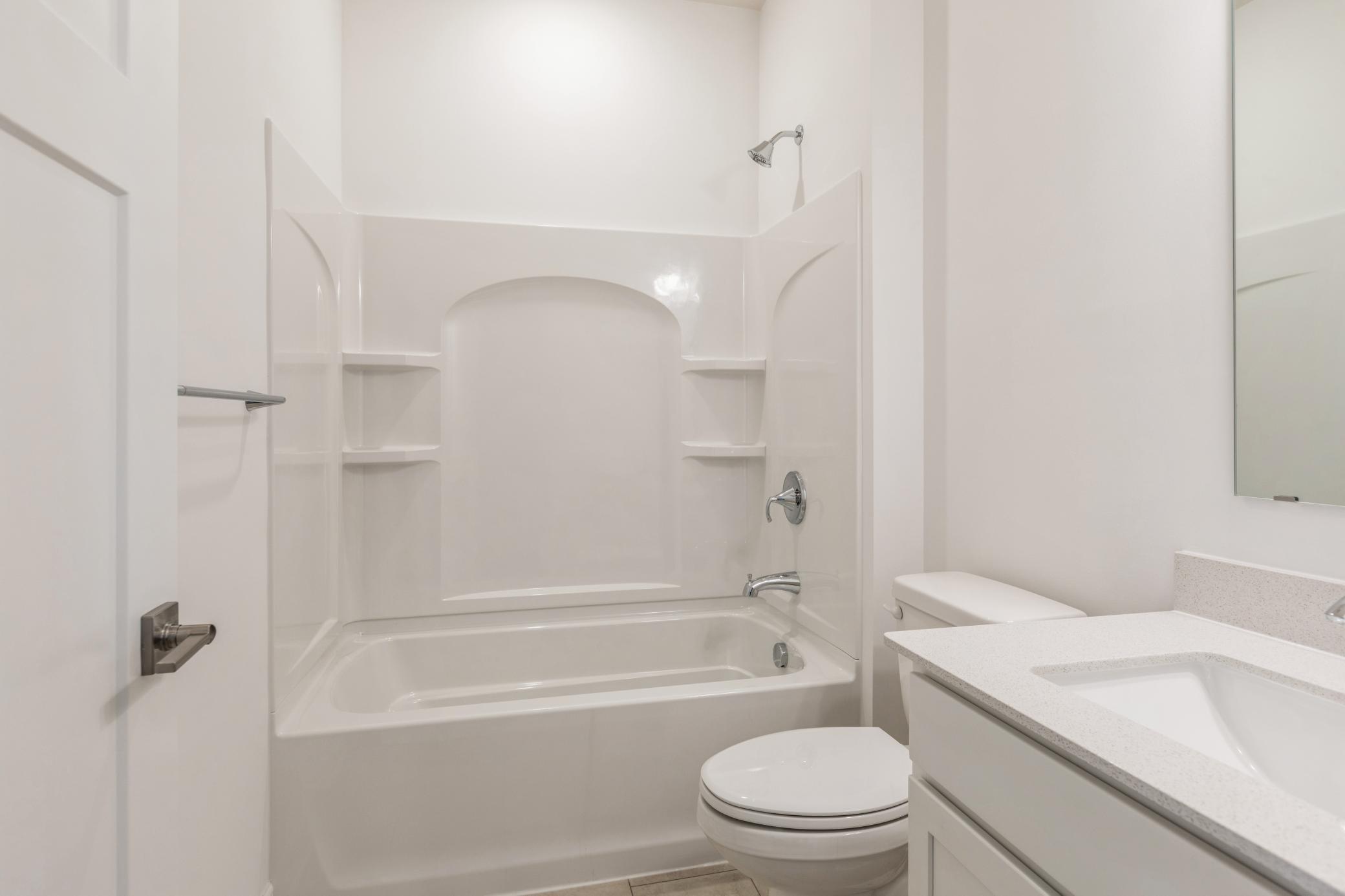 (Photo of a similar home, actual finishes may vary) Conveniently located alongside the secondary bedroom, this full bathroom features an undermount sink with a Moen® faucet and a combination tub and shower with built-in shelves.