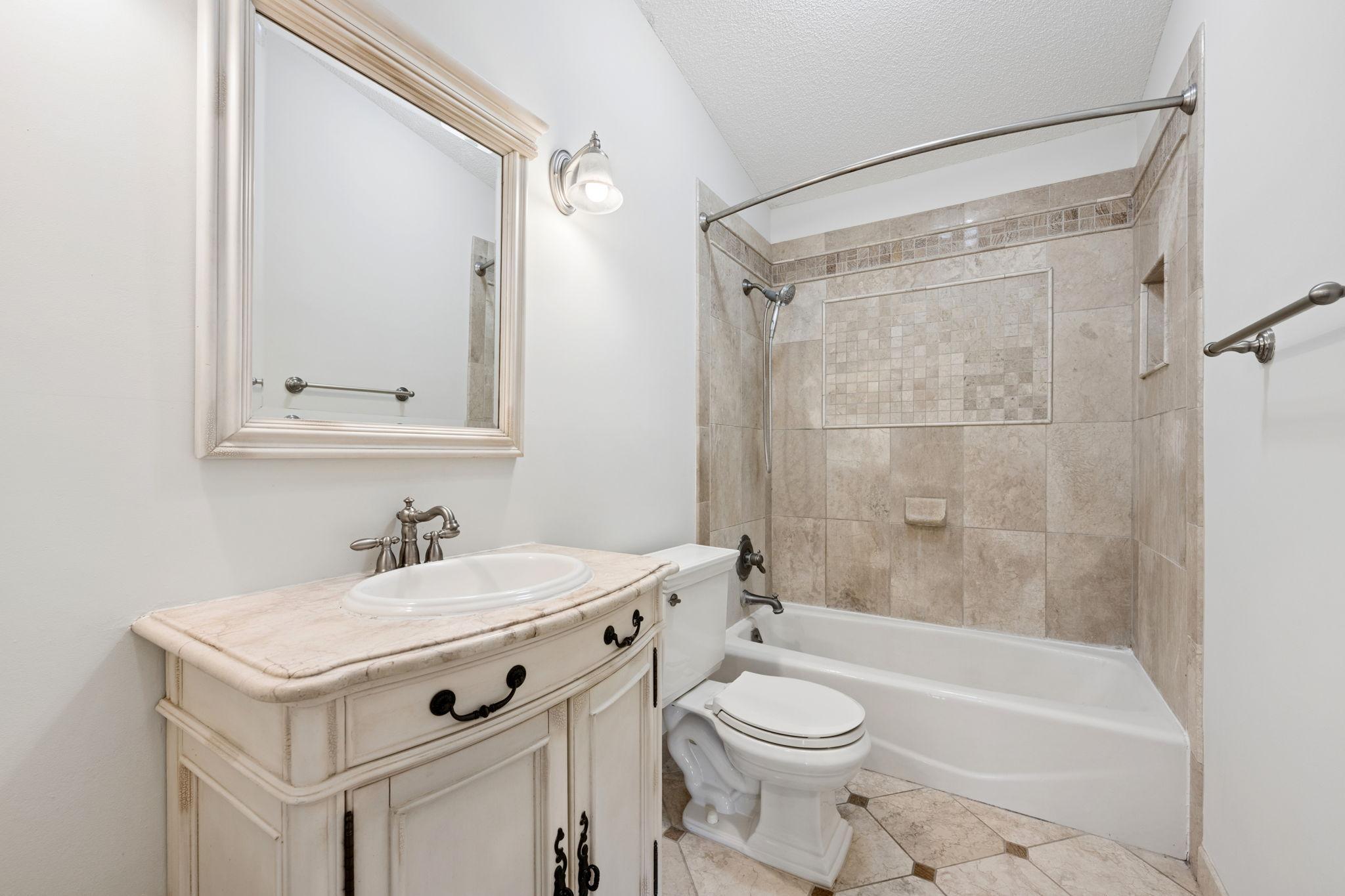 Full bathroom on upper level with antique vanity and tiled shower.