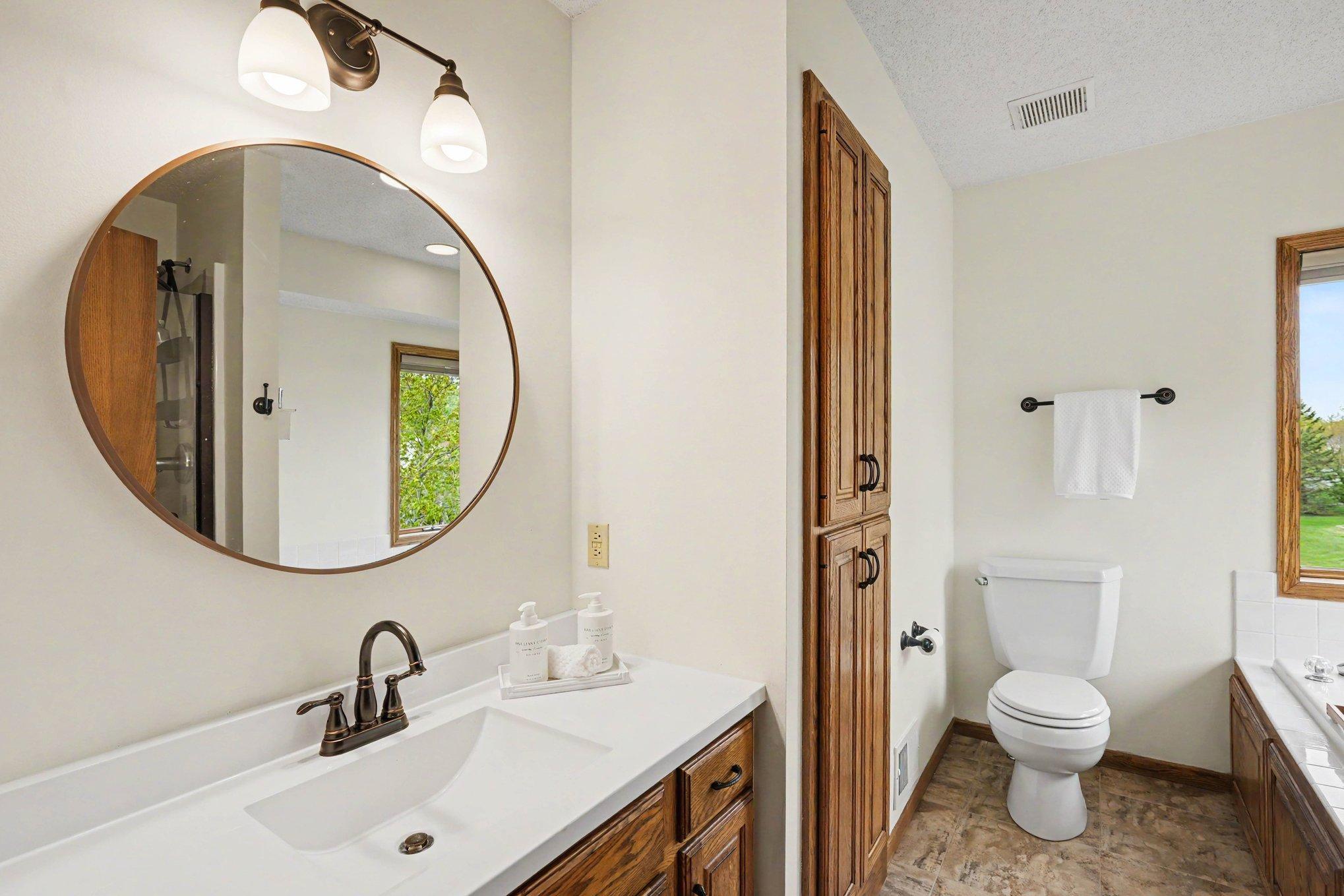 This view of the private full bath showcases the sleek vanity with a seamless sink and a convenient, deep linen closet. A clean, organized space designed for effortless morning routines.