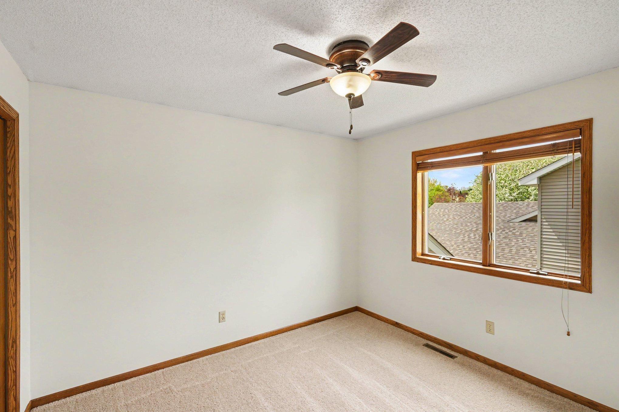 View of the second bedroom on the upper level. It features brand new carpet, a ceiling fan, a large window & a roomy closet.