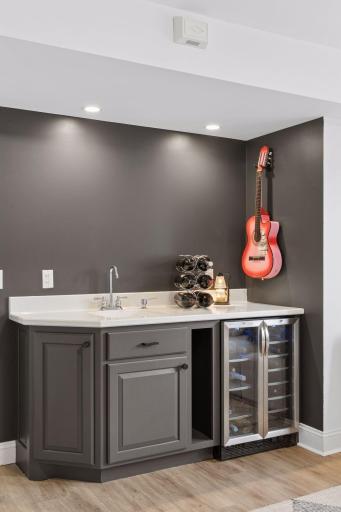 Stylish lower level wet bar with sink, cabinetry, and beverage fridgeâperfect for entertaining. Dark accent walls add a modern touch to this cozy gathering space.