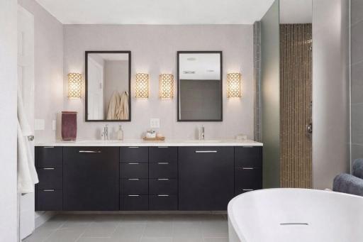 Spa-like primary bath with a long dual vanity, sleek modern cabinetry, and elegant wall sconces. A glass shower and freestanding soaking tub create a relaxing retreat.