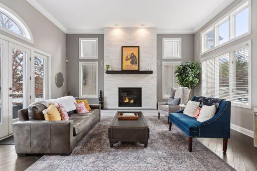 Stunning living room featuring a dramatic fireplace wall, tall windows, and elegant crown molding. French doors provide seamless access to the outdoor living space