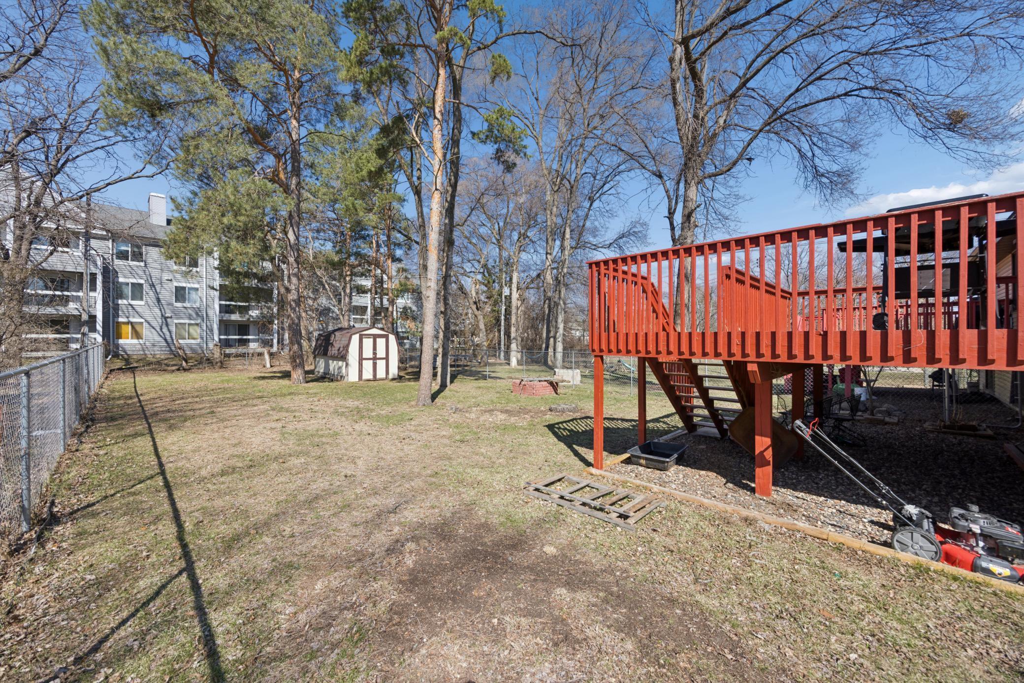 Fully fenced backyard with mature trees, storage shed and fire pit