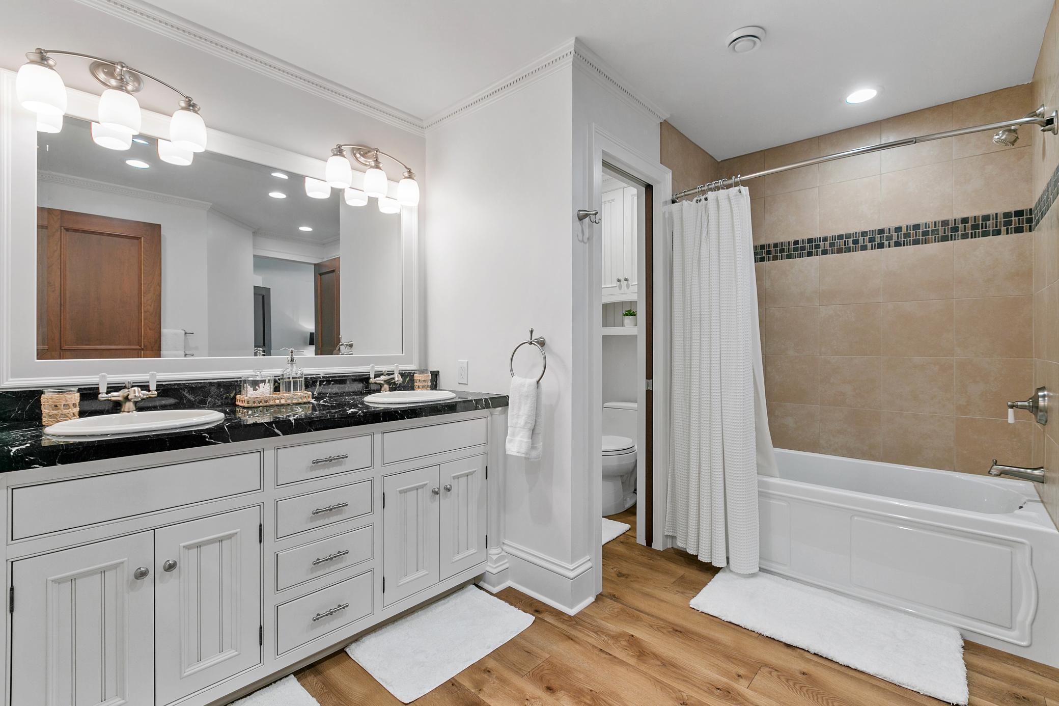 Spacious bathroom featuring double sinks, a bathtub, and a separate stool room.