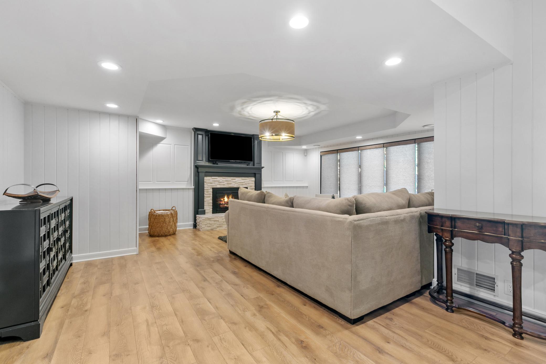 Basement recreation room also has a cozy fireplace, shiplap detail and easy to care for wood floors.
