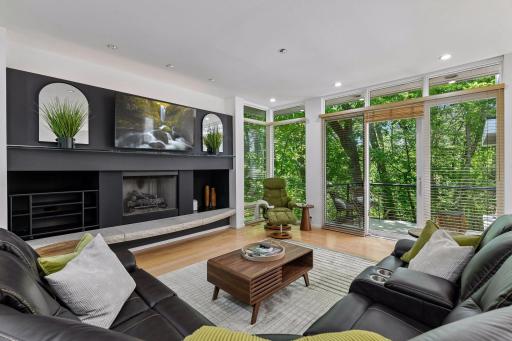 The Family Room brings warmth and architectural character with rich wood floors, a stone-hearth gas fireplace, and expansive windows framing the surrounding landscape.