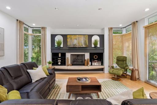The Family Room brings warmth and architectural character with rich wood floors, a stone-hearth gas fireplace, and expansive windows framing the surrounding landscape.