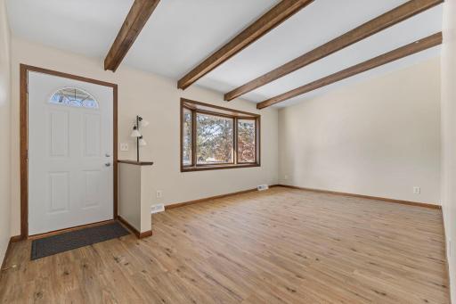 As you enter into the living room, you're greeted by neutral tones, vaulted ceilings with wood beams, and abundant natural light.