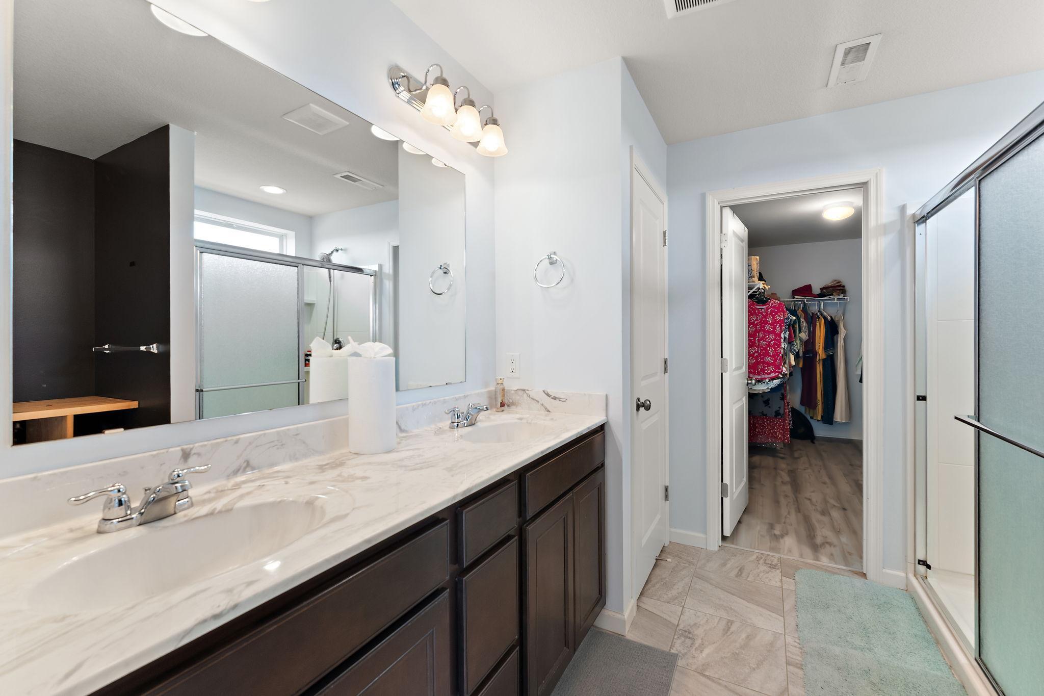 The spa-like primary ensuite boasts a dual-sink vanity with ample storage, modern fixtures, and a clean, bright aesthetic with a massive walk in closet.