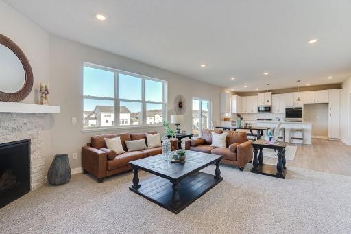 The generously sized family room features a gas fireplace with a stone surround and white mantel. The wood flooring from the kitchen will extend through the living room in this home. Photo of model home, colors and finishes will vary.