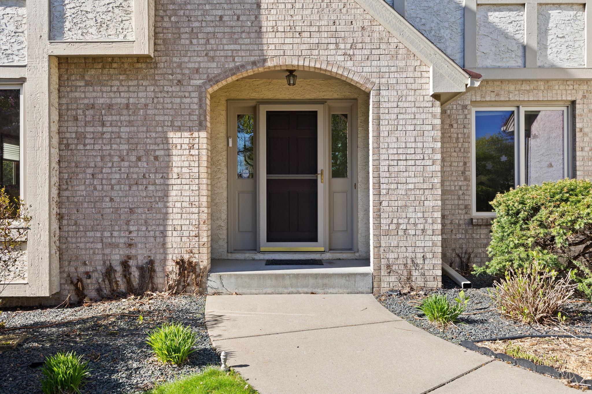 A memorable entrance framed with timeless, neutral brick, concrete walkway and established landscape.