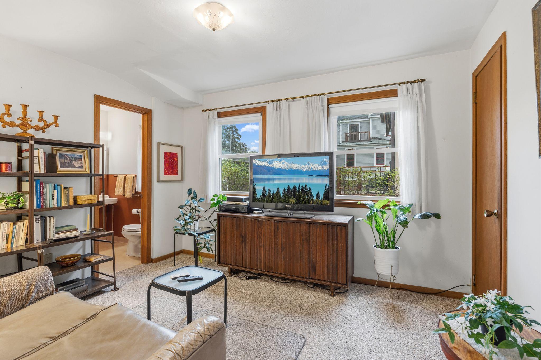 This flexible main floor bedroom is currently used as a TV room, highlighting its potential as a guest space or home office. It features direct access to a half-bath for added convenience.