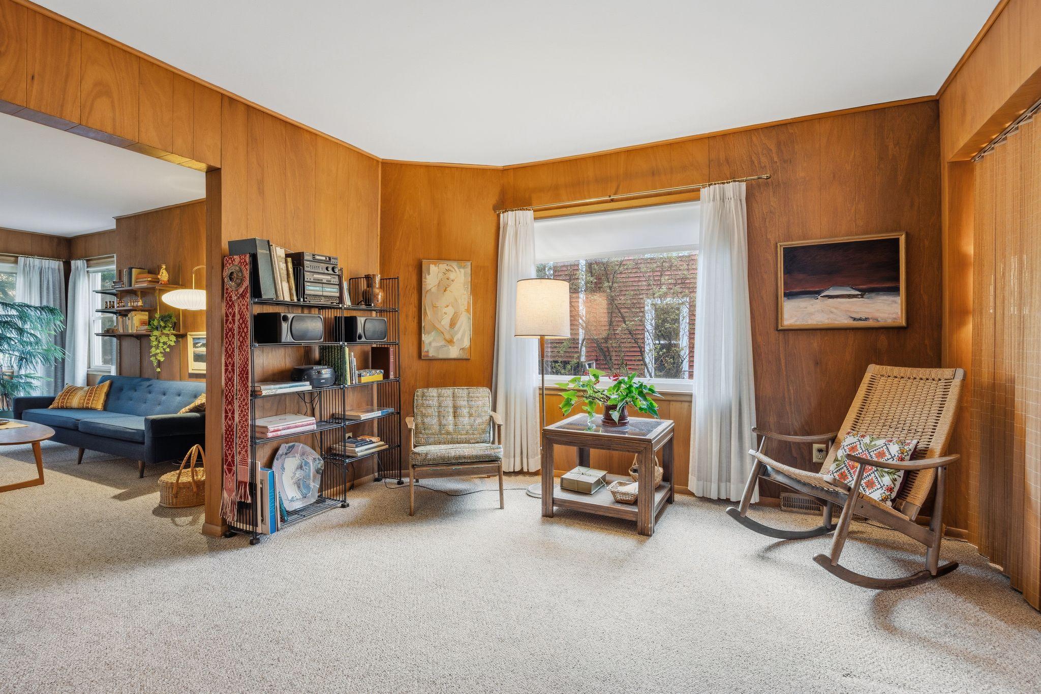 The authentic teak walls continue into this versatile sitting room, creating a warm and cohesive mid-century aesthetic. Large windows fill the space with natural light, highlighting the home's unique architectural blend.