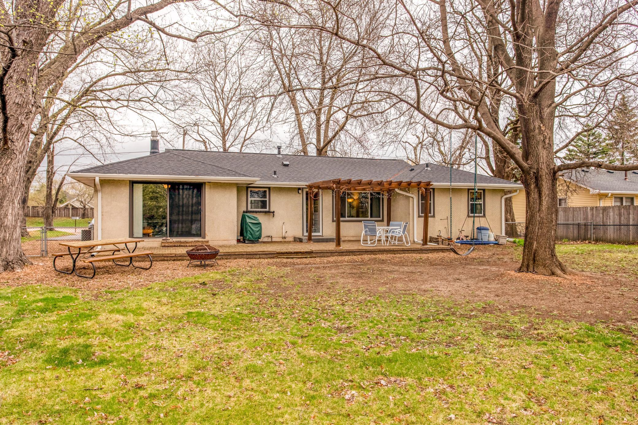 Spacious, fully fenced backyard featuring mature trees, a large patio, and a pergola—perfect for outdoor entertaining and relaxation.