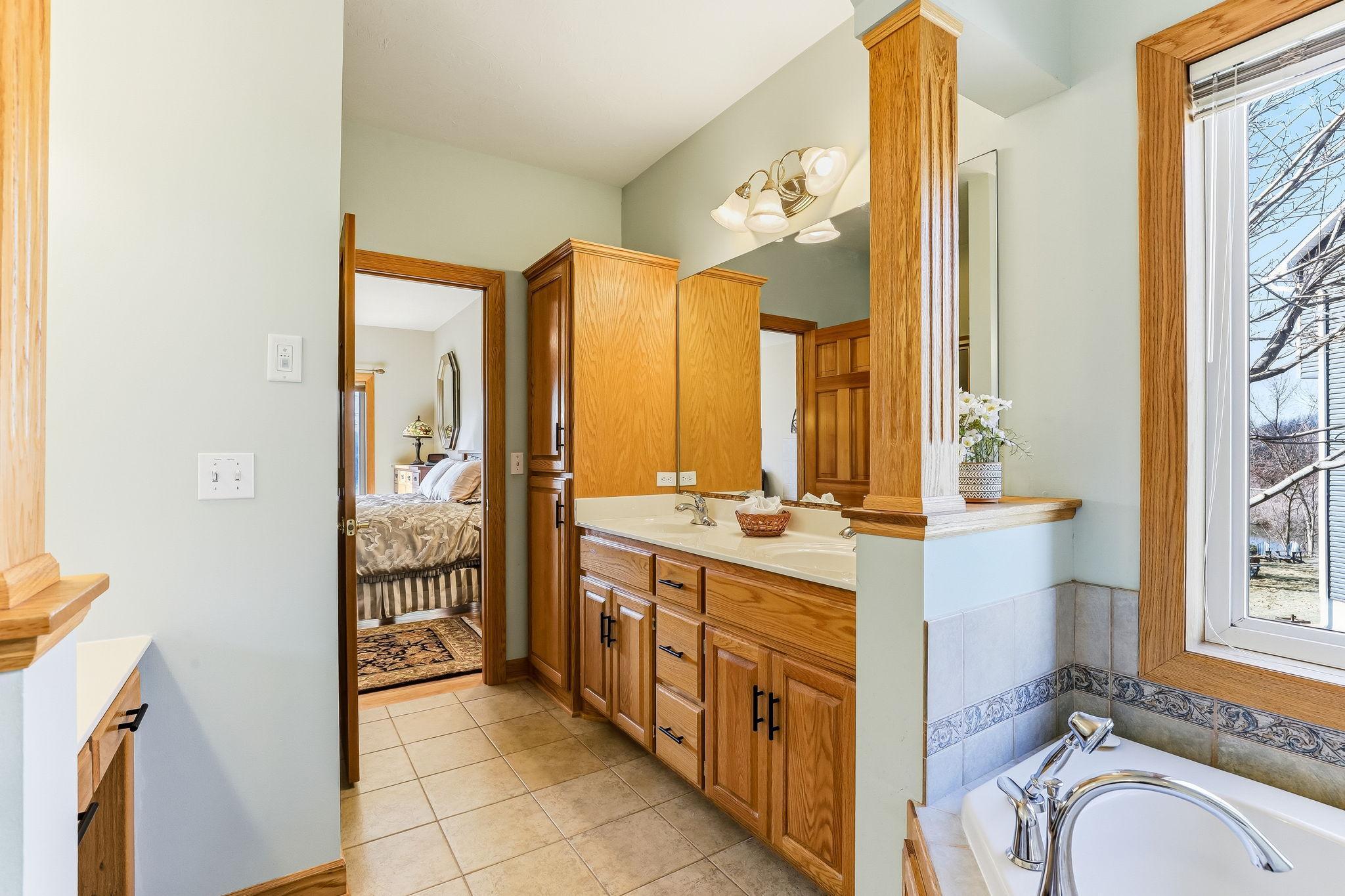 Spacious owner’s bath featuring a jetted tub, separate shower, dual vanities, and tile floors.
