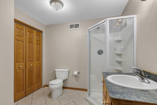 Three-quarter bathroom featuring a custom oak vanity, tiled flooring, and a linen closet.