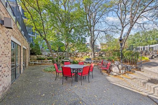 Outdoor gathering space with seating, grilling area, and mature trees.