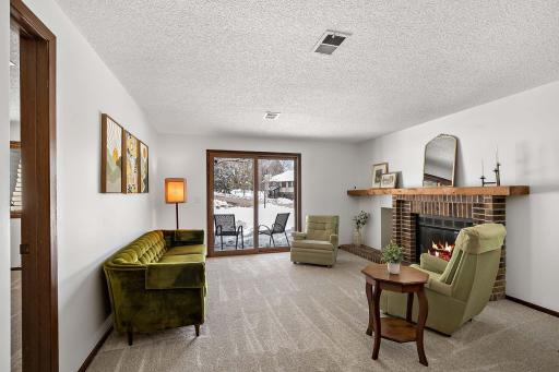 Lower-level family room with abundant natural light, a wood-burning brick fireplace, and a sliding door leading to the patio.