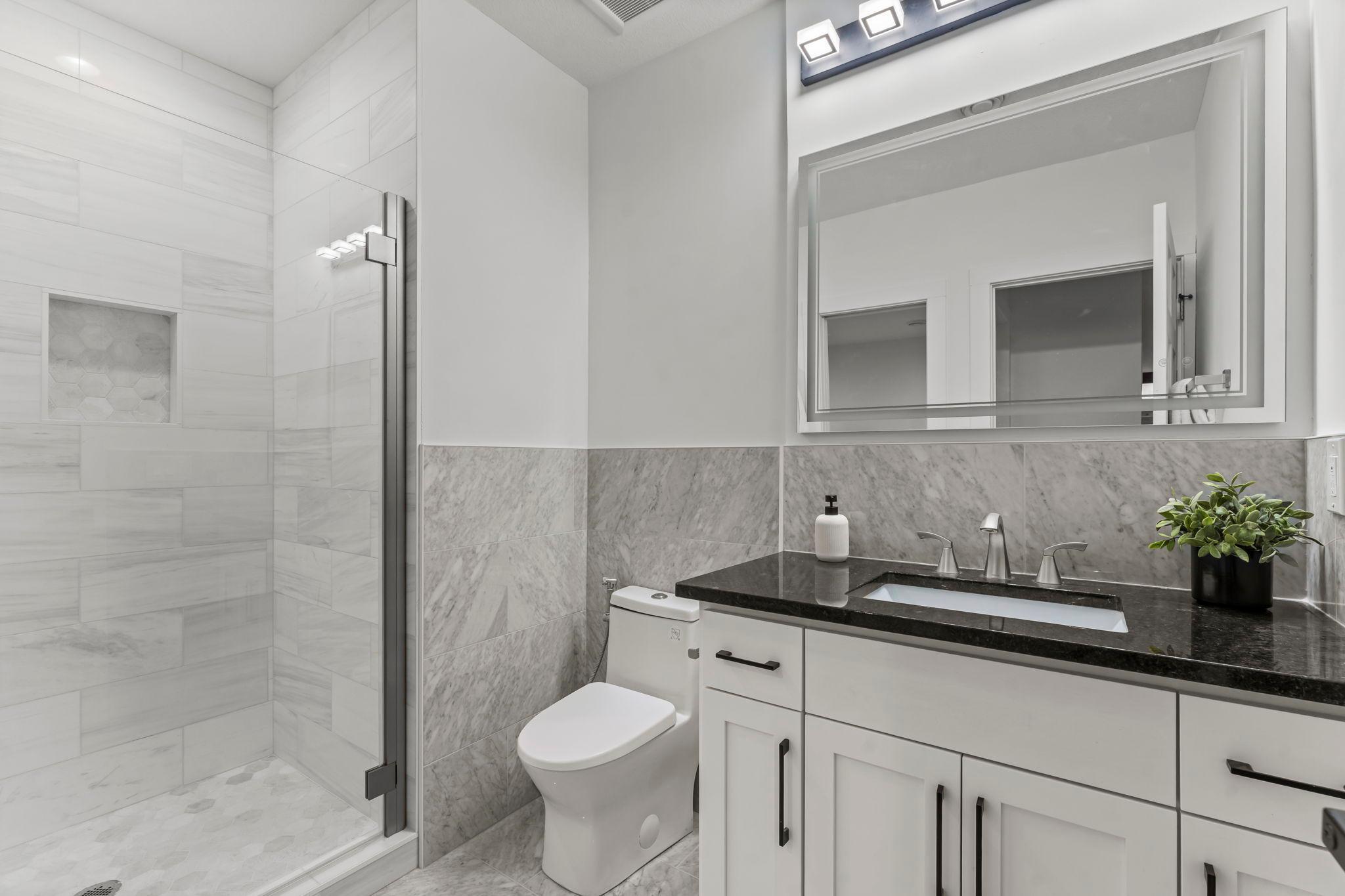 The lower level bathroom features sleek, modern finishes including a black quartz vanity and a beautiful marble floors with marble-accented walls.