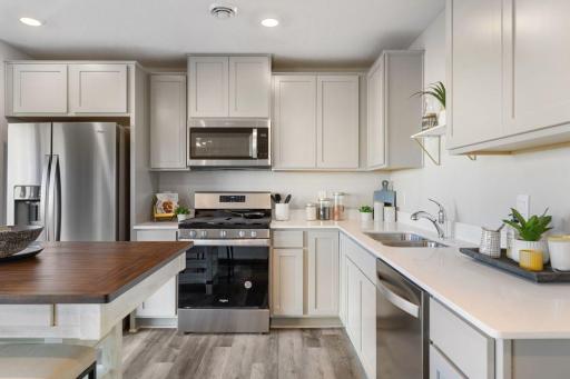 Modern kitchen with light gray cabinets, quartz countertops and stainless appliances. Model photos. Options and colors will vary.
