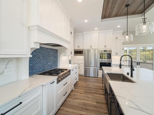 This kitchen was designed with matching quartz backsplash to blend into the countertops then an accent of mosaic stone behind the large 6 burner gas cooktop grill. Overhead range hood is buried/hidden in the cabinetry in this kitchen.