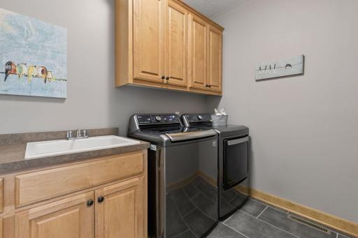 Main floor laundry room with tile floors, cabinets and utility sink.