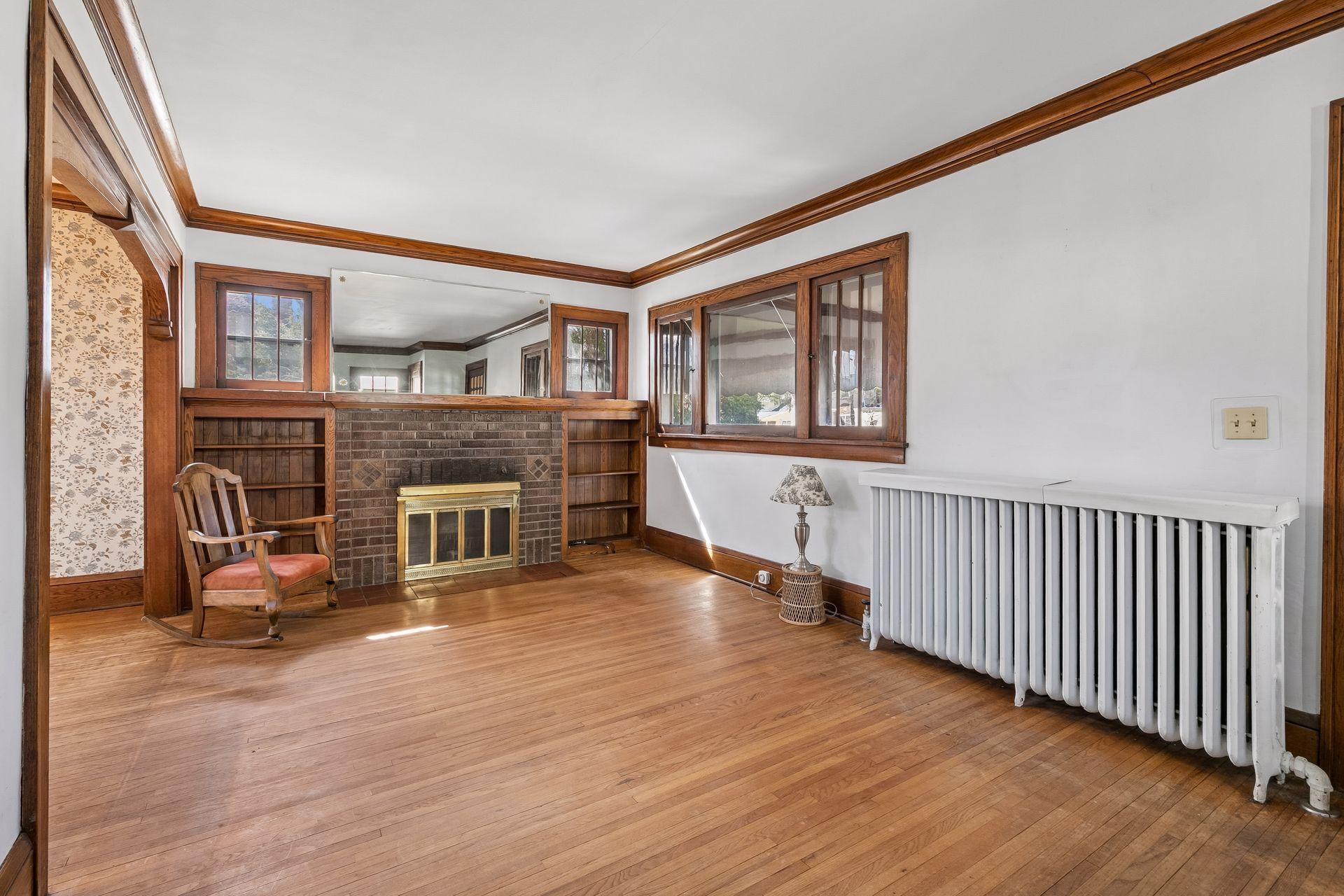 Comfortable living space with hardwood floors, a charming brick wood-burning fireplace, built-in bookshelves, and plentiful windows for airy comfort.