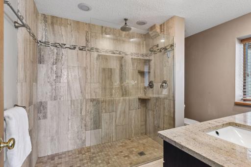 Primary lower level bathroom features dual vanities and tiled walk in shower