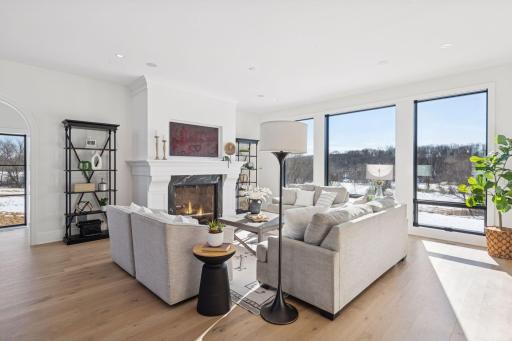 Elegant living room with soaring windows, beautiful hardwood floors, and a statement fireplaceâoffering abundant natural light and peaceful outdoor views.