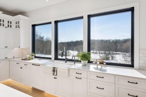 Designer kitchen with large panoramic windows, farmhouse sink, quartz surfaces, and crisp white cabinetry, all perfectly positioned to capture serene outdoor views.