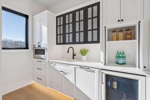 Well-appointed prep kitchen with designer cabinetry, glass display cabinets, bar sink, beverage cooler, and built-in combination convection microwave, ideal for hosting and everyday convenience.