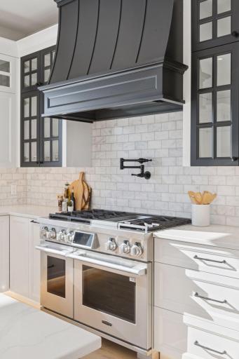 Stunning chefâs kitchen showcasing a high-end gas range, statement custom hood, elegant tile backsplash, and beautiful quartz surfaces.