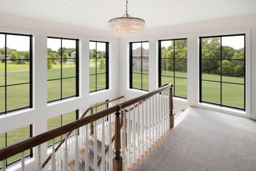 Stunning staircase landing with dramatic windows, elegant chandelier lighting, and sweeping views of the property.