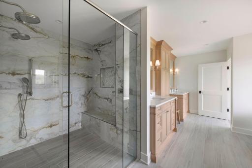 Spa-inspired primary bathroom featuring a large walk-in glass shower with tiled surround and dual vanities with custom cabinetry.