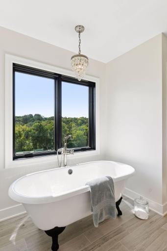 Elegant freestanding soaking tub framed by large windows and peaceful nature views, creating a true spa-like retreat.