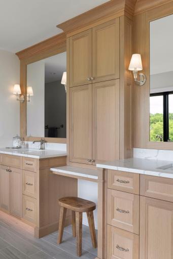Sophisticated primary bathroom with dual vanities, warm custom cabinetry, and a built-in vanity space.