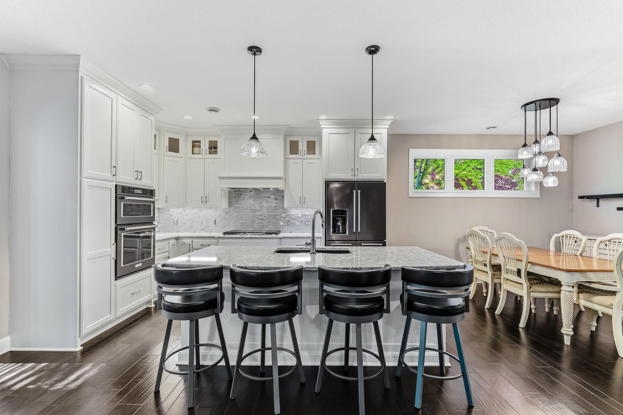 The impressive kitchen features quartz countertops, glass backsplash, upgraded appliances, and custom enameled cabinetry with crown molding.