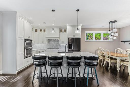 The impressive kitchen features quartz countertops, glass backsplash, upgraded appliances, and custom enameled cabinetry with crown molding.
