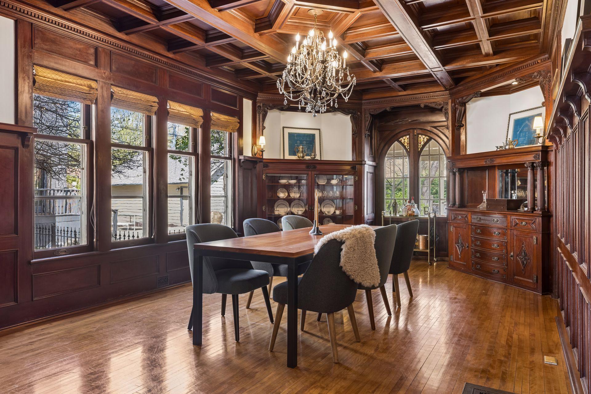 Stunning formal dining room with exquisite original woodwork, coffered ceiling, custom built-ins, and a statement chandelier. Walls of windows fill the space with natural light, creating a warm and sophisticated setting for dining and entertaining.