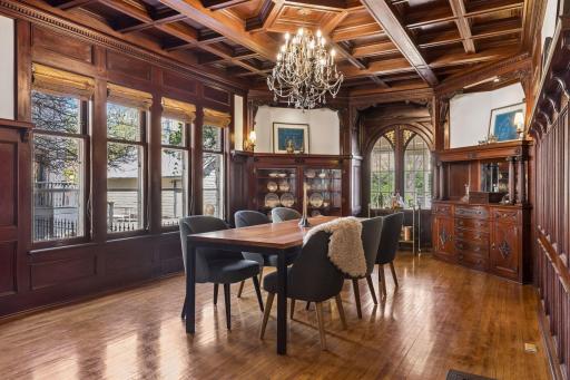 Stunning formal dining room with exquisite original woodwork, coffered ceiling, custom built-ins, and a statement chandelier. Walls of windows fill the space with natural light, creating a warm and sophisticated setting for dining and entertaining.